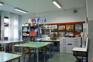 Aula di arte con tavoloni e sedie, lavori realizzati dai ragazzi appesi, armadi per custodire il materiale utile alle attività pratiche.