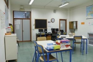 Aula polivalente usata per attività di studio in piccolo gruppo: ci sono diversi tavoli al centro, armadi e librerie, postazioni pc, cartine geografiche, ...