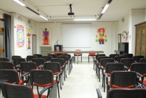 L'aula magna al piano terra ha sedie rosse, un tavolo grande e un videoproiettore con una postazione pc di comando.
